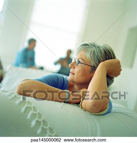 Mature woman sitting on sofa, people sitting in background View Large Photo Image Stock Image - Mature woman sitting on sofa, people sitting in background. Fotosearch