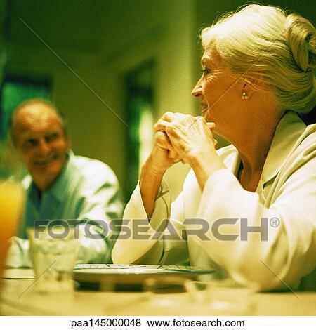 Mature woman sitting with elbows on table, looking at man, low angle view View Large Photo Image Stock Photo - Mature woman sitting with elbows on table, looking at man, low angle view. Fotosearch