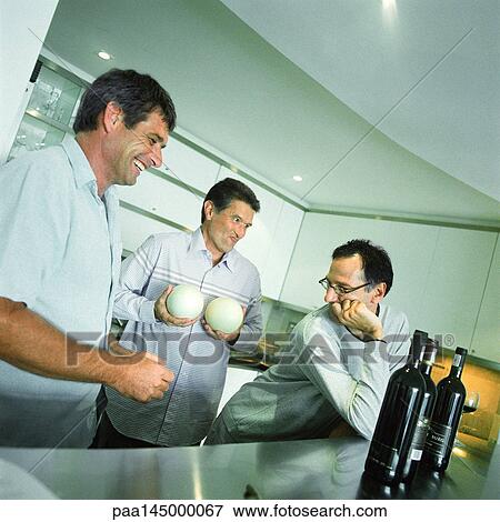 Three men standing in kitchen, one holding melons View Large Photo Image Stock Photo - Three men standing in kitchen, one holding melons. Fotosearch