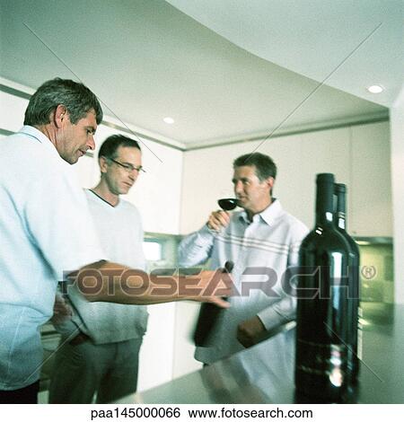 Three men standing in kitchen, one holding glass View Large Photo Image Stock Photograph - Three men standing in kitchen, one holding glass. Fotosearch