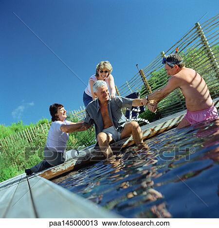 Three people trying to push a man into water View Large Photo Image Stock Image - Three people trying to push a man into water. Fotosearch