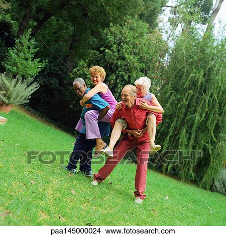 Two mature men giving women piggyback rides, outdoors View Large Photo Image Picture - Two mature men giving women piggyback rides, outdoors. Fotosearch