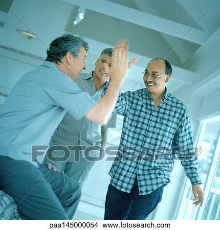 Two mature men slapping hands in air, third man in background View Large Photo Image Picture - Two mature men slapping hands in air, third man in background. Fotosearch