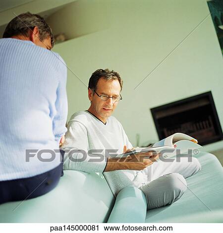 Two men sitting on sofa, one reading View Large Photo Image Stock Image - Two men sitting on sofa, one reading. Fotosearch