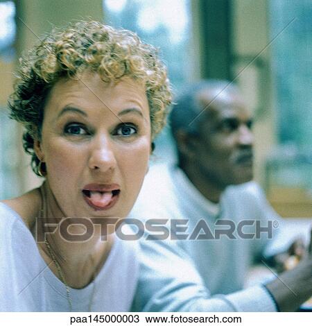 Stock Image - Woman sticking out tongue, man in background. Fotosearch