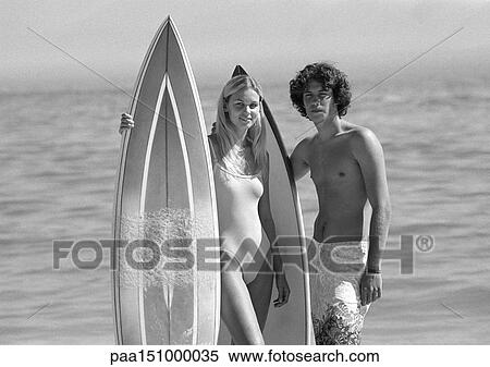 Couple holding surfboards, looking into camera, b&w. View Large Photo Image Stock Photography - Couple holding surfboards, looking into camera, b&w. . Fotosearch