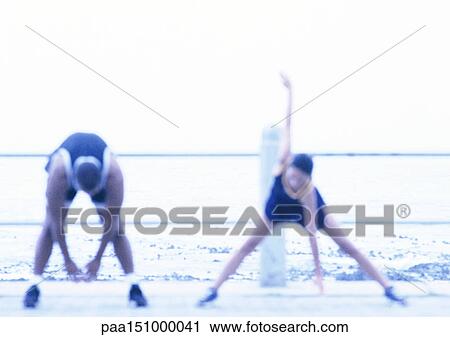 Stock Image - Couple stretching, sea in background, blurred.. Fotosearch