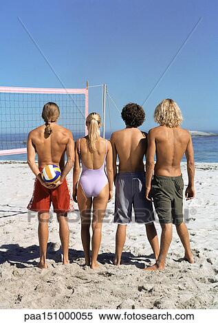 Stock Photography - Four young people standing on beach with volleyball, rear view.. Fotosearch