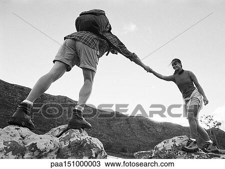 Stock Image - Man helping woman across rocks, low angle view, b&w.. Fotosearch