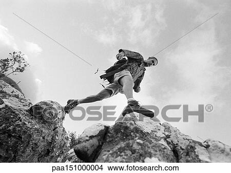 Picture - Man stepping across rocks, low angle view, b&w.. Fotosearch