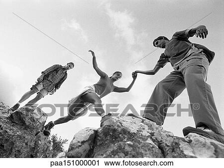 Three young people climbing on rocks, woman being aided, low angle view, b&w. View Large Photo Image Stock Image - Three young people climbing on rocks, woman being aided, low angle view, b&w.. Fotosearch