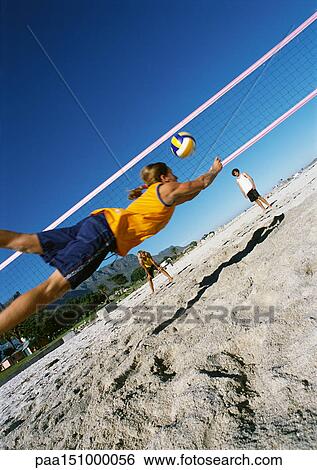 Three young people playing beach volleyball, one mid-air. View Large Photo Image Stock Photograph - Three young people playing beach volleyball, one mid-air.. Fotosearch