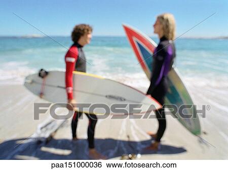 Two young men holding surfboards on the beach, facing each other, blurred. View Large Photo Image Stock Photograph - Two young men holding surfboards on the beach, facing each other, blurred.. Fotosearch