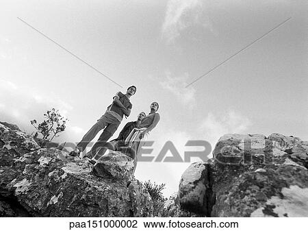 Stock Image - Two young people standing on rocks, low angle view, b&w.. Fotosearch