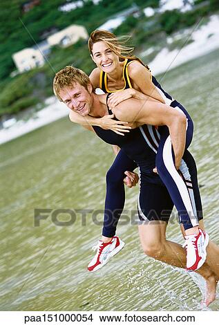 Picture - Young couple on beach, woman on man's back.. Fotosearch