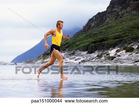 Young man jogging through water, mountains in background. View Large Photo Image Picture - Young man jogging through water, mountains in background.. Fotosearch