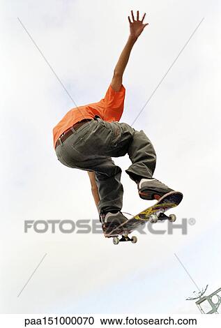 Young man on skateboard, jumping, mid-air, low angle, rear view. View Large Photo Image Stock Image - Young man on skateboard, jumping, mid-air, low angle, rear view.. Fotosearch