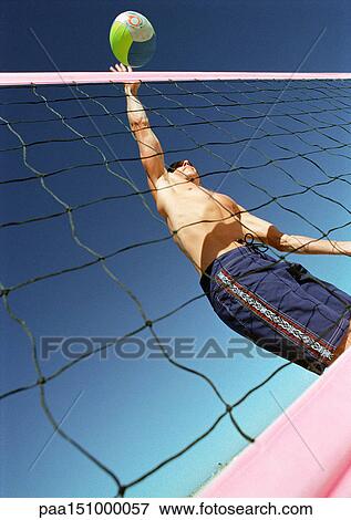 Young man playing beach volleyball, hitting ball over net, low angle view. View Large Photo Image Stock Photo - Young man playing beach volleyball, hitting ball over net, low angle view.. Fotosearch
