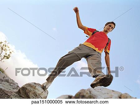 Stock Photography - Young man stepping across rocks, low angle view.. Fotosearch