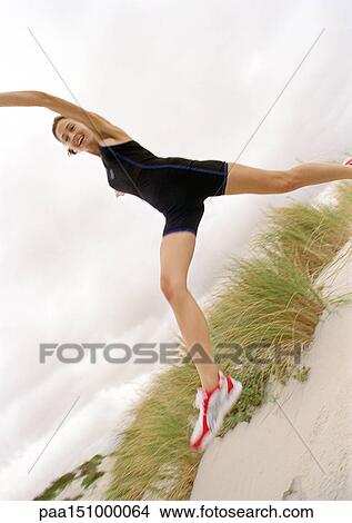 Picture - Young woman on beach, jumping, looking into camera, low angle view.. Fotosearch