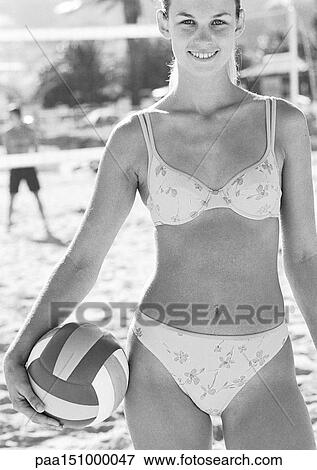 Stock Photo - Young woman smiling on beach, holding volleyball, portait, b&w.. Fotosearch