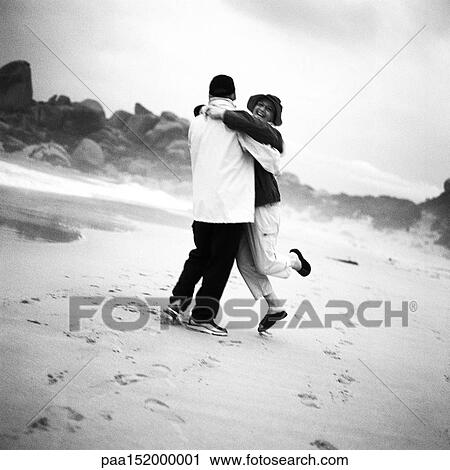 Stock Image - Couple smiling, hugging on beach, b&w.. Fotosearch