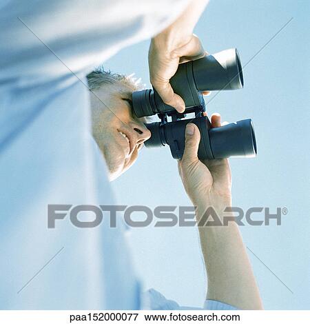 Stock Photo - Man looking through binoculars, low angle view. Fotosearch