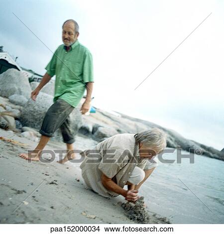 Mature couple on beach, woman digging. View Large Photo Image Picture - Mature couple on beach, woman digging.. Fotosearch