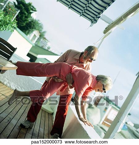 Stock Image - Mature couple playing on deck of beach house.. Fotosearch