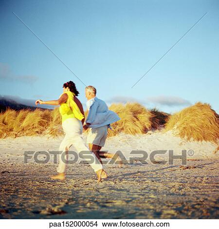 Picture - Mature couple running on beach, side view.. Fotosearch
