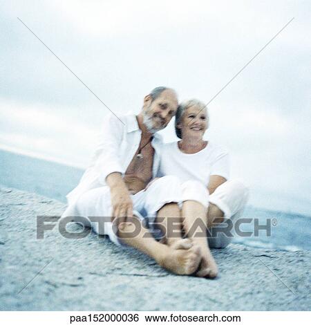 Mature couple sitting on beach, looking into camera. View Large Photo Image Stock Photograph - Mature couple sitting on beach, looking into camera.. Fotosearch
