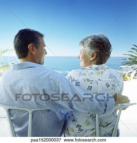 Mature couple sitting on beach, man's arm around woman, rear view. View Large Photo Image Stock Photo - Mature couple sitting on beach, man's arm around woman, rear view.. Fotosearch