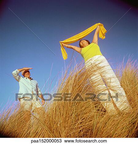 Mature couple standing in tall grass, woman holding scarf above head. View Large Photo Image Stock Image - Mature couple standing in tall grass, woman holding scarf above head.. Fotosearch