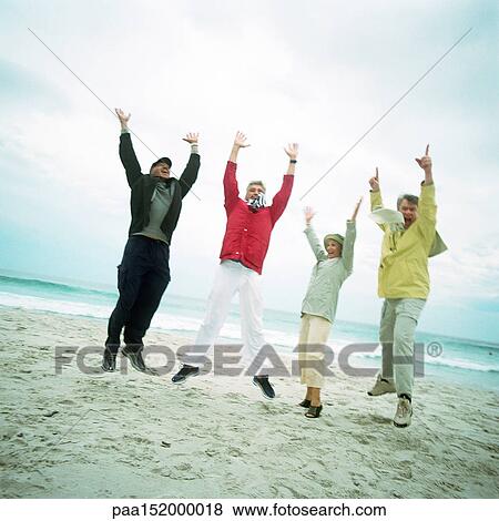 Stock Photo - Mature group on beach, jumping in air, looking into camera.. Fotosearch