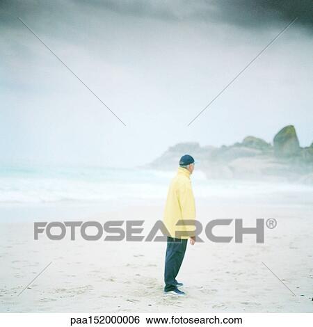 Stock Photograph - Mature man standing on beach, side view.. Fotosearch