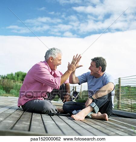 Mature men sitting together, slapping hands in air, on deck outside View Large Photo Image Stock Image - Mature men sitting together, slapping hands in air, on deck outside. Fotosearch