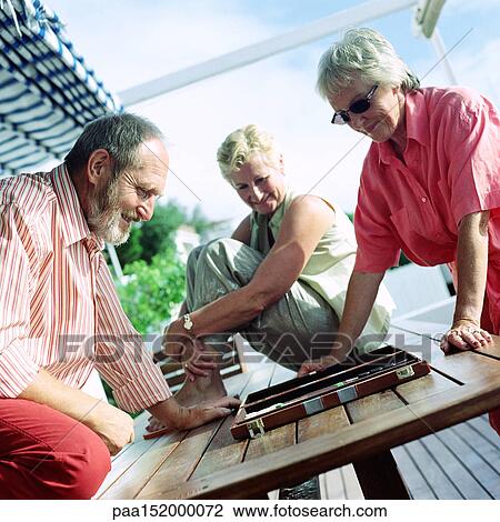 Stock Image - Three mature adults playing backgammon.. Fotosearch