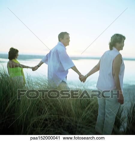Three mature friends holding hands on beach, rear view. View Large Photo Image Stock Image - Three mature friends holding hands on beach, rear view.. Fotosearch