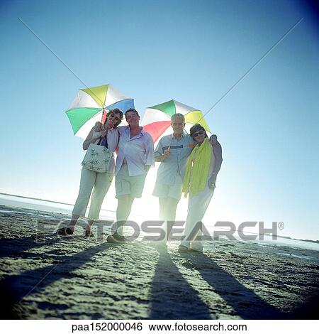 Two mature couples standing on beach, holding umbrellas. View Large Photo Image Stock Photograph - Two mature couples standing on beach, holding umbrellas.. Fotosearch