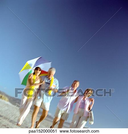 Two mature couples walking on beach, woman holding umbrella. View Large Photo Image Stock Image - Two mature couples walking on beach, woman holding umbrella.. Fotosearch