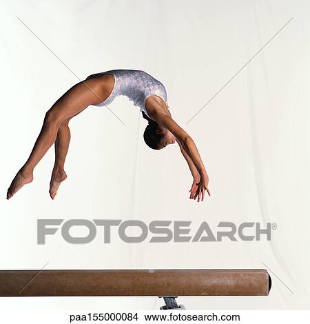 Young female gymnast on balance beam performing, mid-flight, side view. View Large Photo Image Picture - Young female gymnast on balance beam performing, mid-flight, side view.. Fotosearch