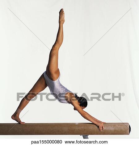 Stock Image - Young female gymnast on balance beam performing, side view.. Fotosearch
