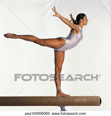 Stock Image - Young female gymnast on balance beam performing, side view.. Fotosearch