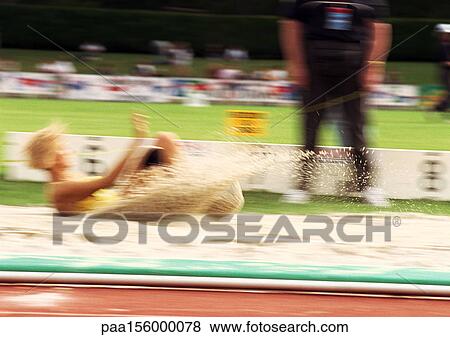 Stock Photo - Female long jumper landing in sand pit, blurred motion. Fotosearch