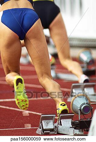 Female runners leaving starting blocks, rear view Stock Photo