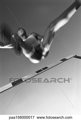 Stock Photo - male athlete jumping hurdle, low angle view, blurred motion, b&w. Fotosearch