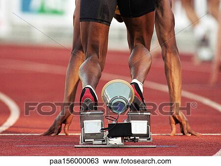 Stock Image - Male runner on starting block, low section, rear view. Fotosearch