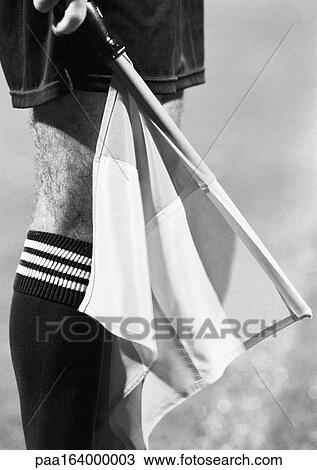 Stock Image - Linesman in soccer match holding flag, close-up of leg and flag, b&w.. Fotosearch
