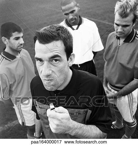 Stock Photo - Referee holding whistle in front of three players, looking into camera, b&w. . Fotosearch