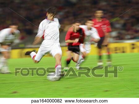 Stock Image - Soccer player about to kick ball, four players in background, blurred.. Fotosearch